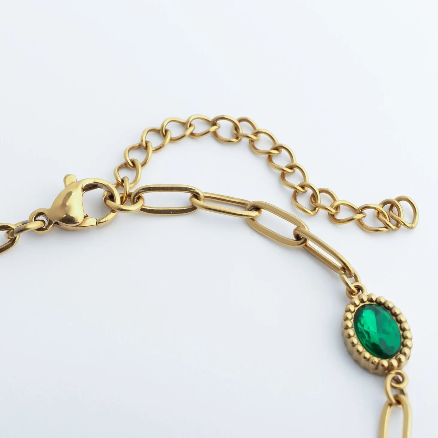 Gold bracelet with a green gemstone on a white background