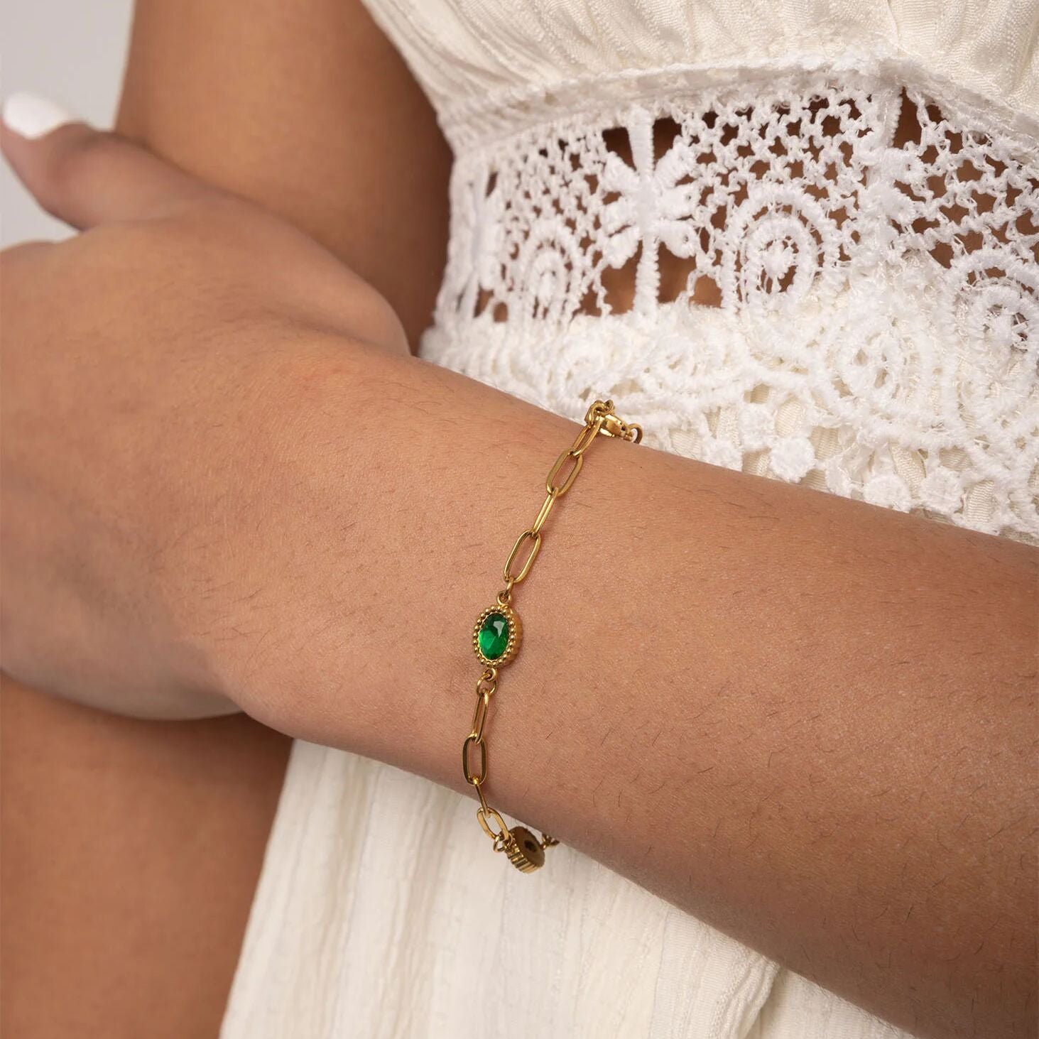 Gold bracelet with a green gemstone on a person's wrist wearing a white lace top.