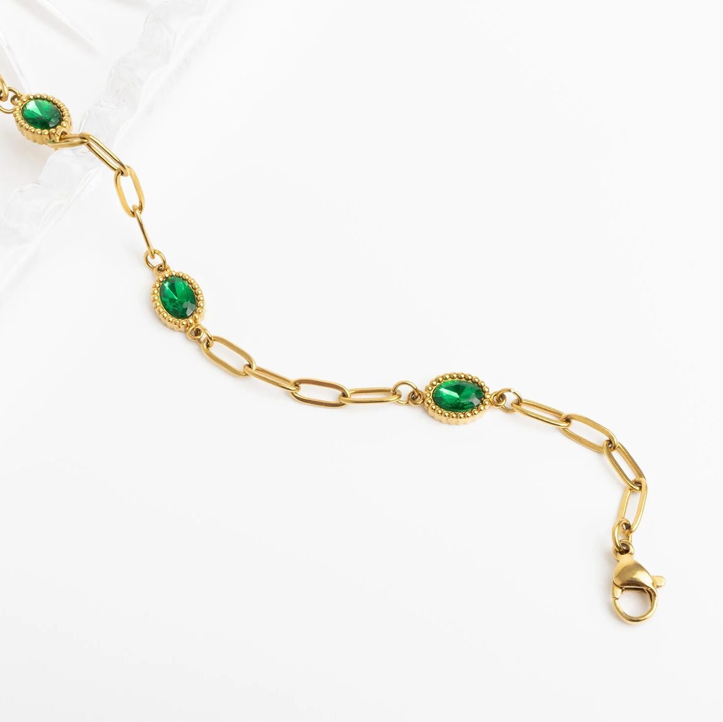 Gold bracelet with green gemstones on a white background