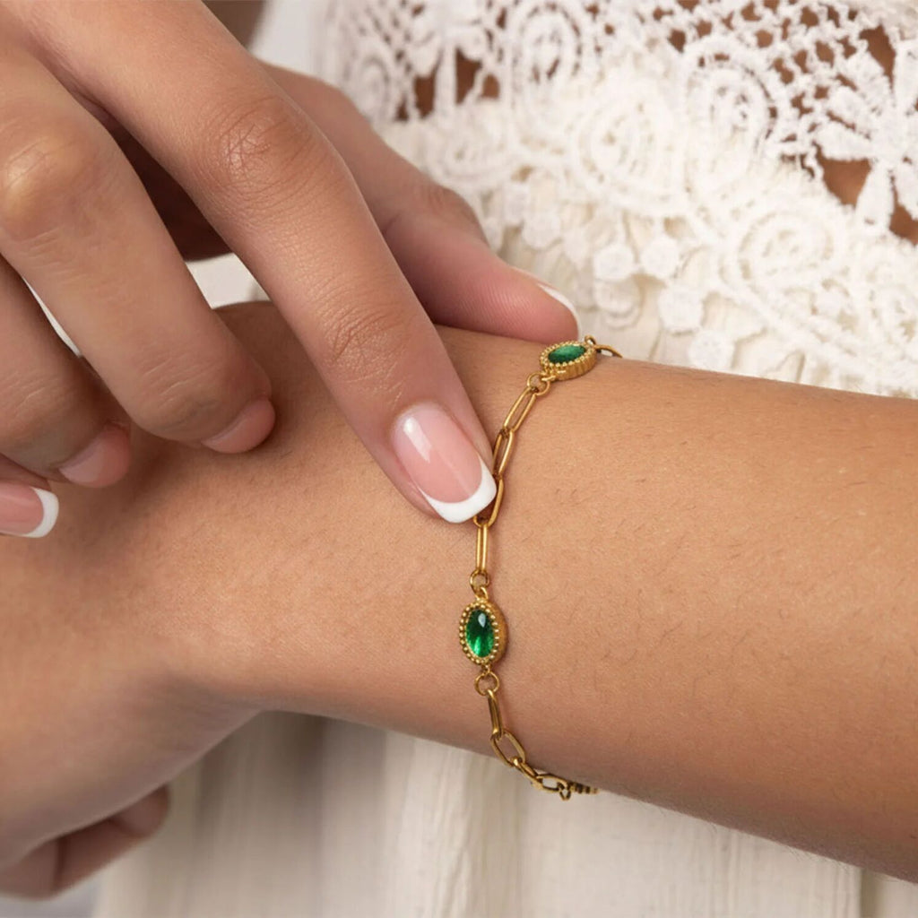 Gold bracelet with green gemstones on a wrist against a white lace background