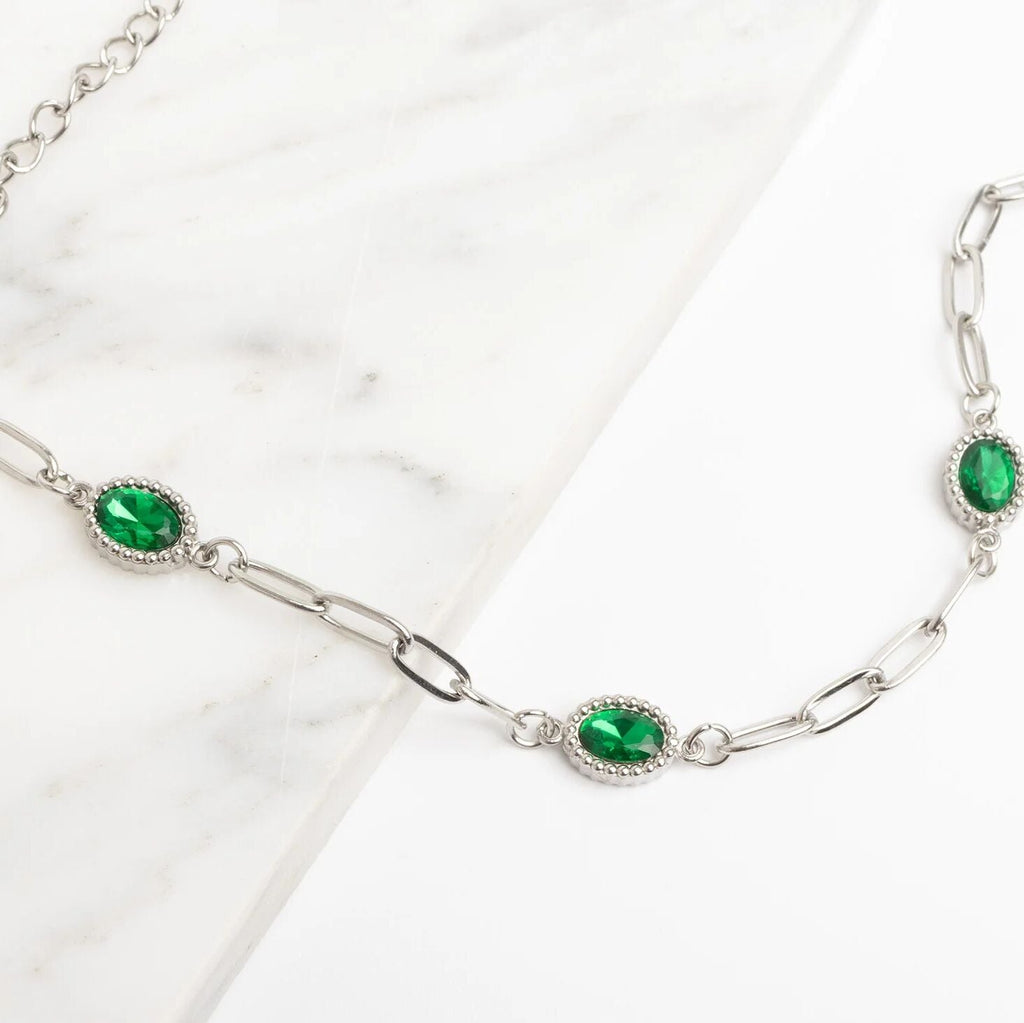 Silver chain necklace with green gemstones on a white background
