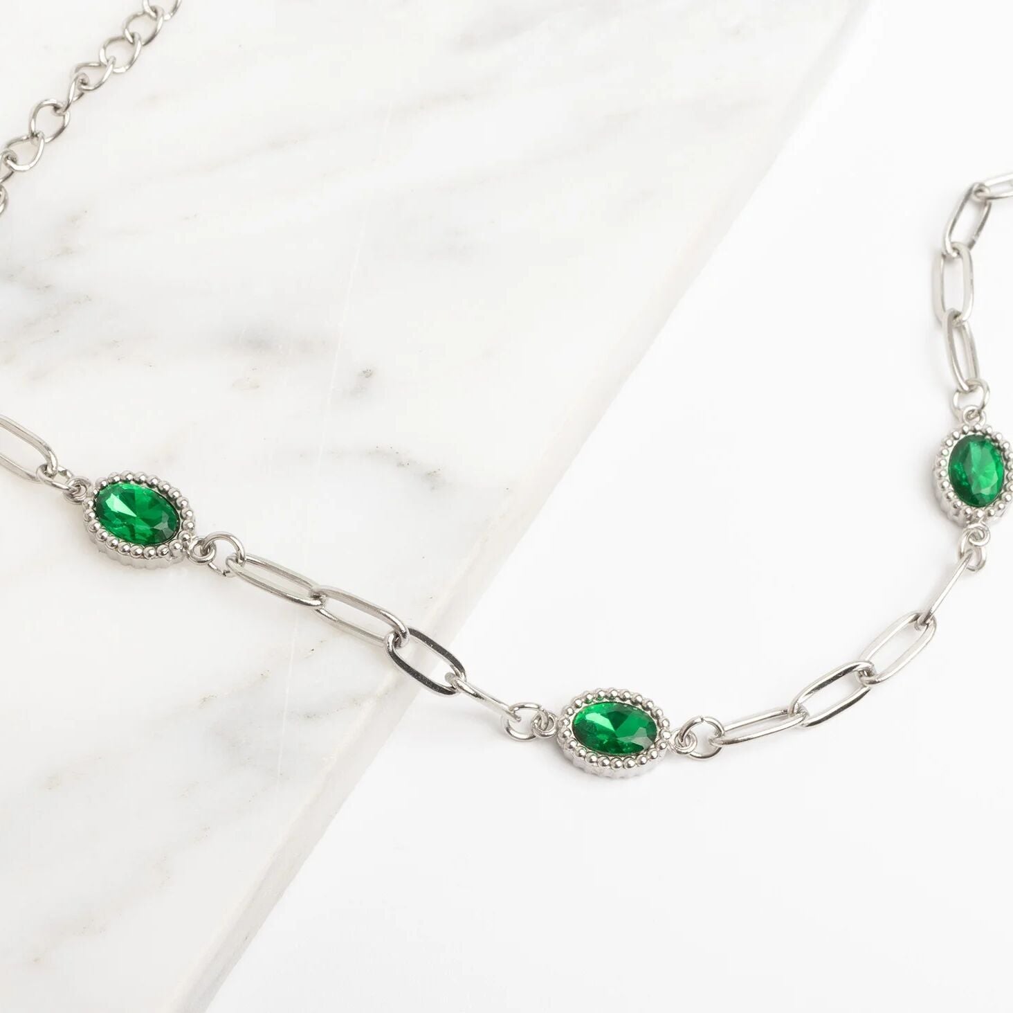 Silver chain necklace with green gemstones on a white background