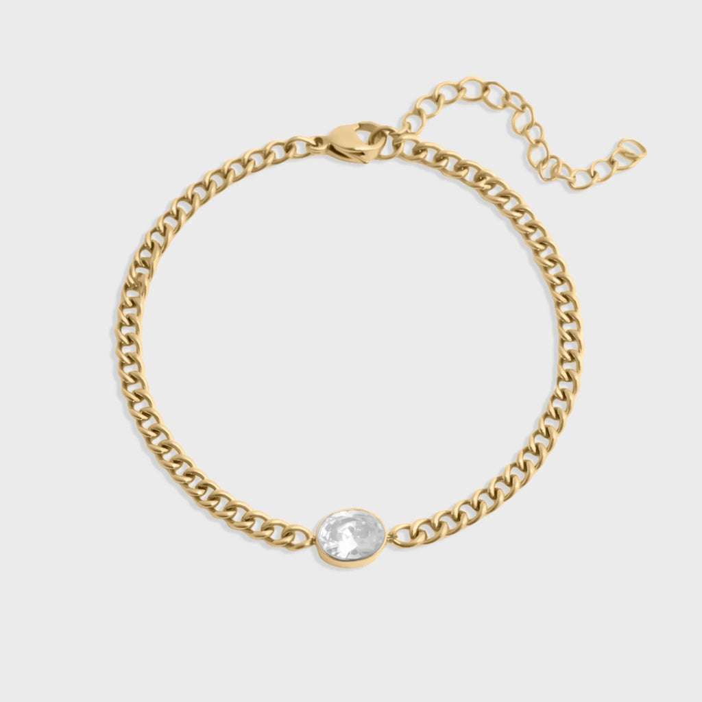 Gold chain bracelet with a clear gemstone on a light gray background