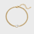 Gold chain bracelet with a clear gemstone on a light gray background