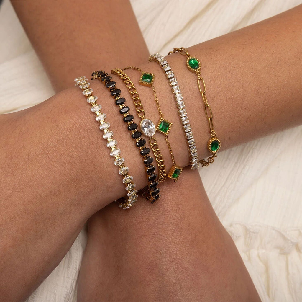 Close-up of a wrist wearing multiple bracelets with green gemstones on a light background