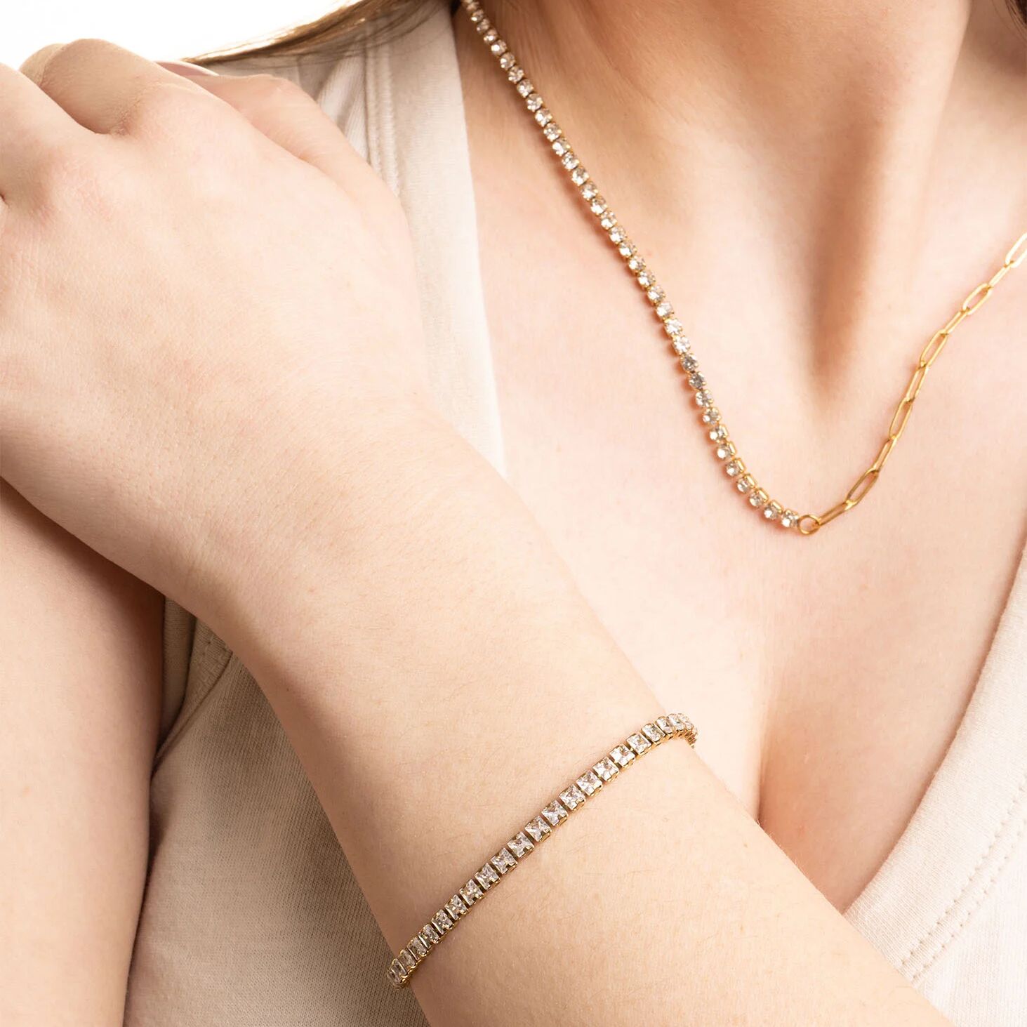 Close-up of a person wearing a gold necklace and bracelet on a plain background