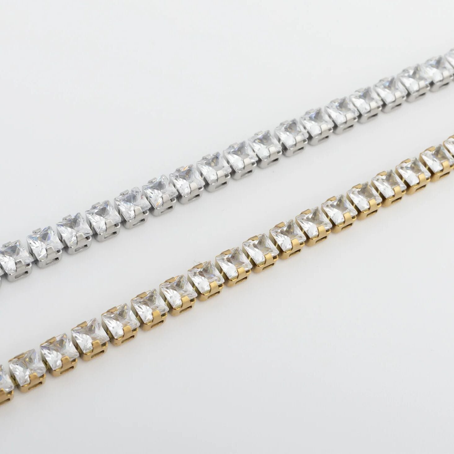 Two strands of clear rhinestone chains, one silver and one gold, on a light gray background.