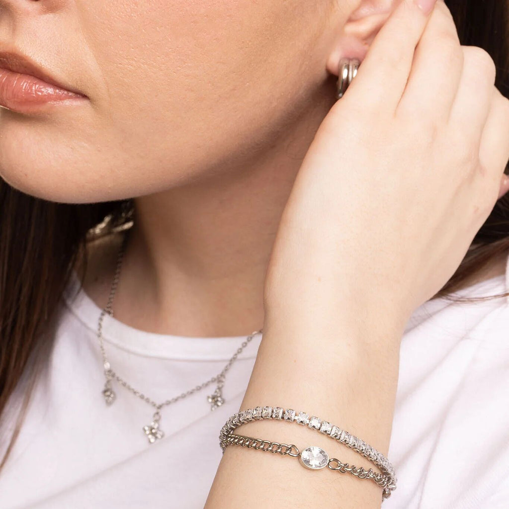 Close-up of a woman wearing silver jewelry including an earring, necklace, and bracelet.