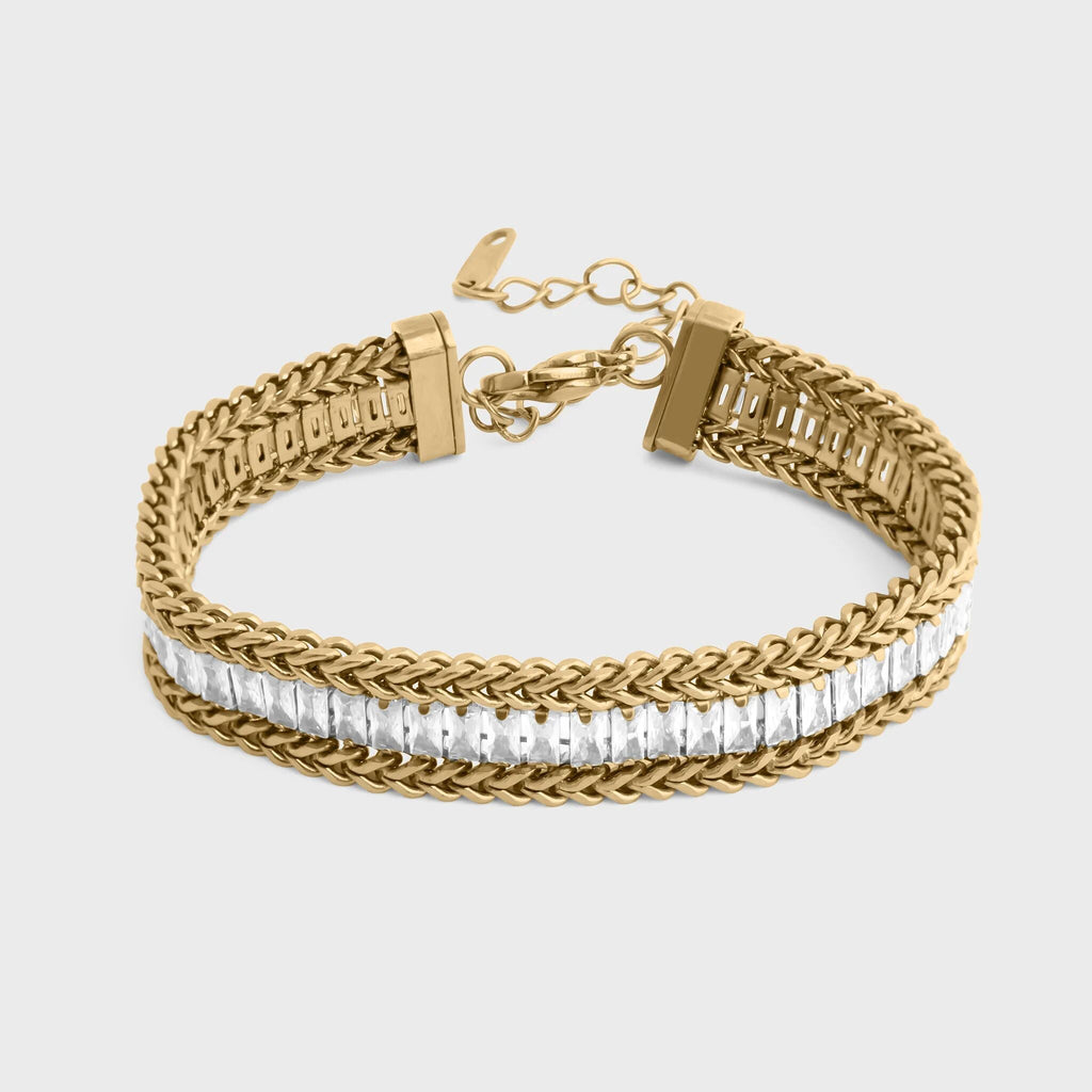 Gold bracelet with braided design and clear stones on a light gray background