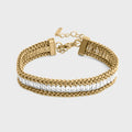 Gold bracelet with braided design and clear stones on a light gray background