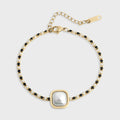 Gold bracelet with a central pearl and black gemstones on a white background