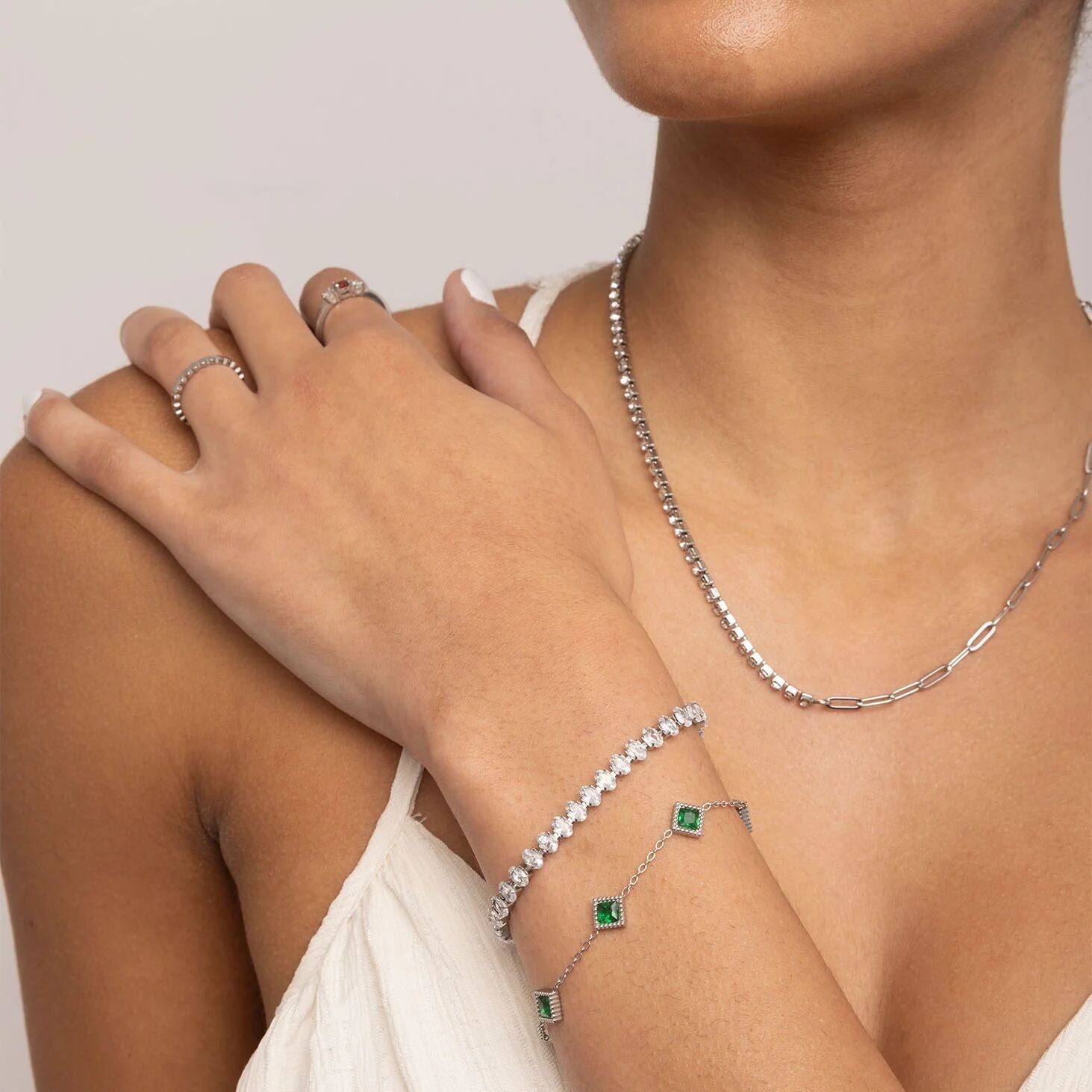 Person wearing silver jewelry including a necklace, bracelet, and ring on a plain background