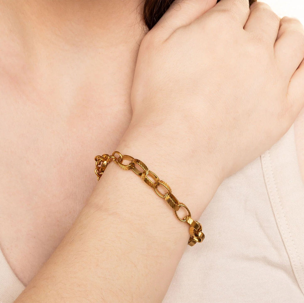 Gold chain bracelet on a person's wrist with a neutral background