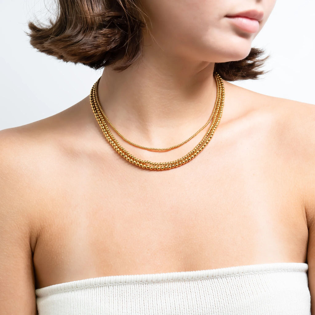 Gold beaded necklace on a person against a white background