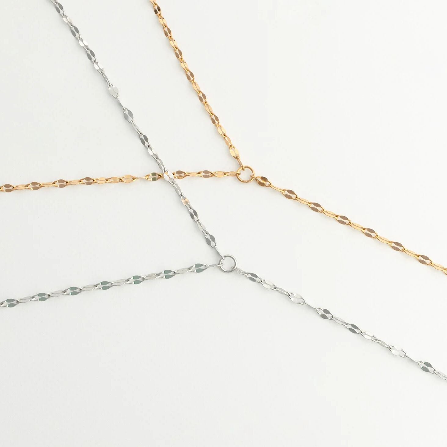 Three gold and silver Full Body Lip Chains intersecting on a light gray background