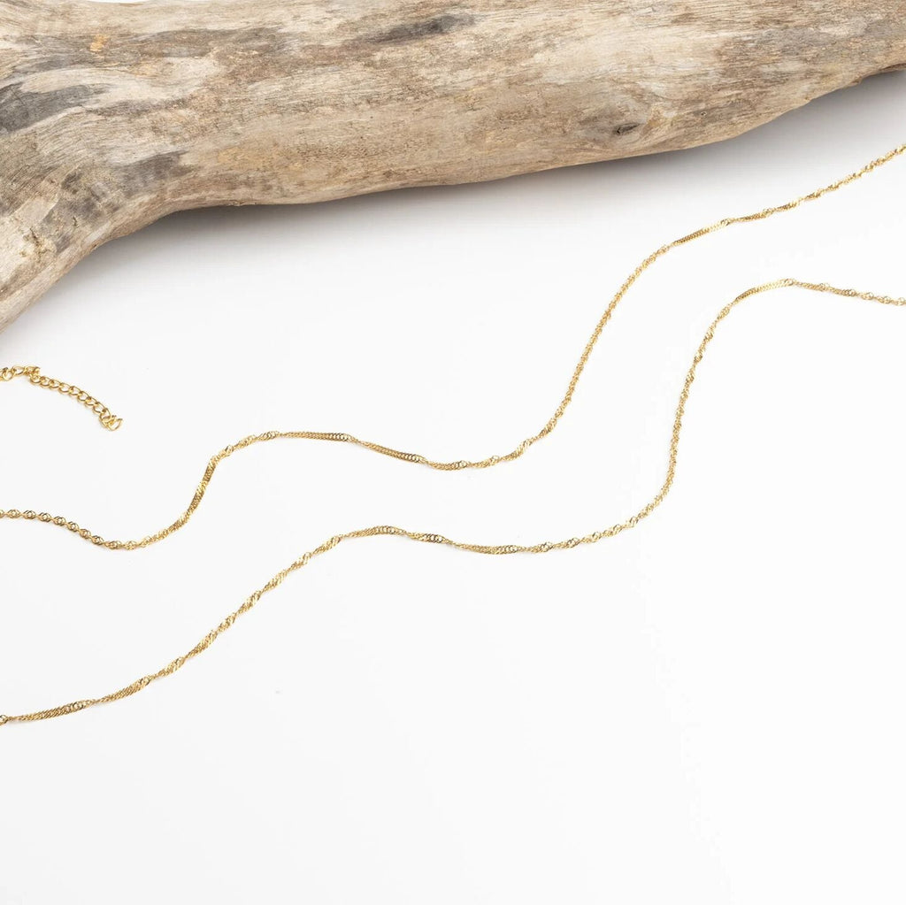 Gold Singapore Belly Chain on a white surface with a piece of driftwood.