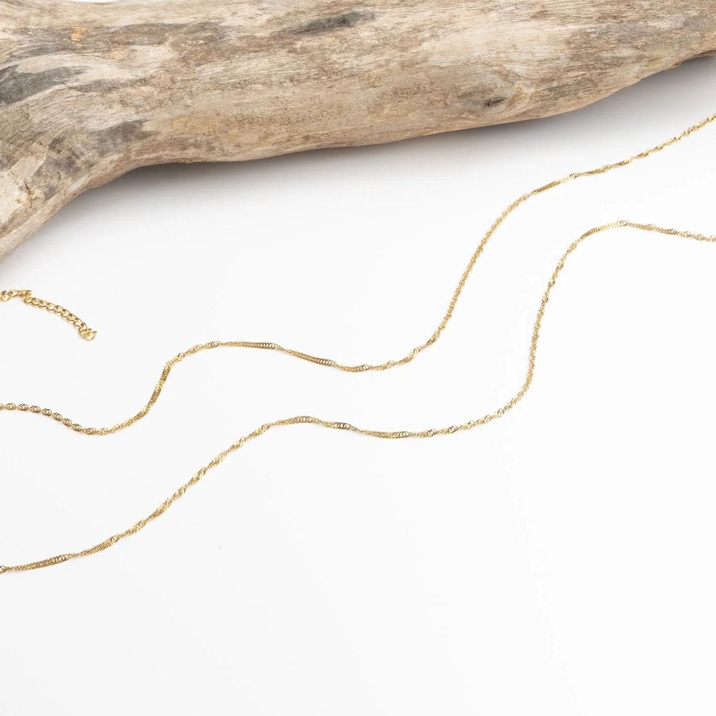 Gold Singapore Belly Chain on a white surface with a piece of driftwood.