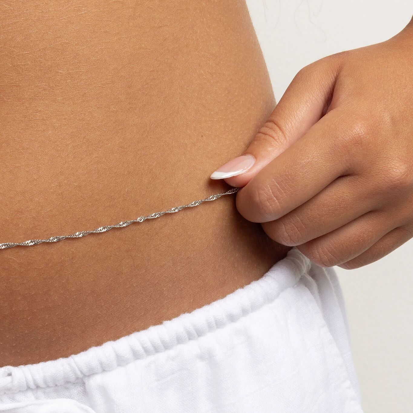 Person wearing a silver Singapore Belly Chain around their waist with a hand adjusting it.
