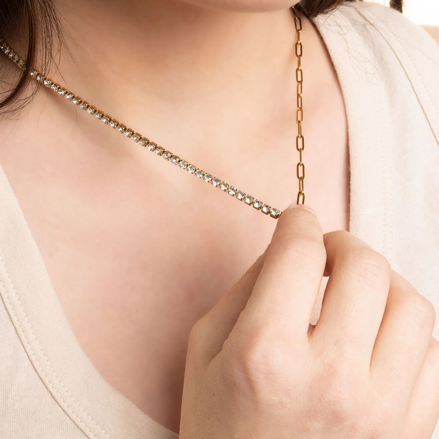 Gold chain necklace being adjusted by a hand on a light background