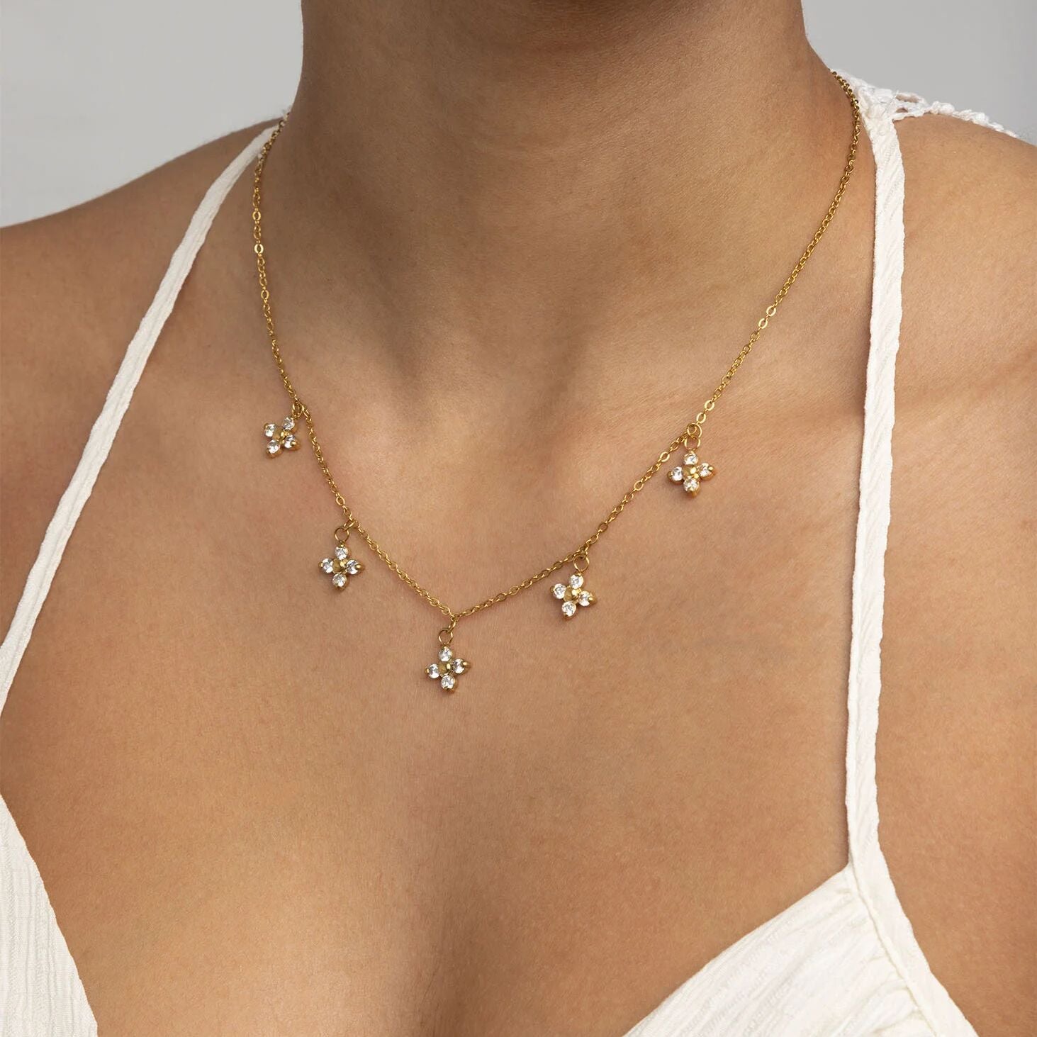 Gold necklace with floral pendants on a person wearing a white top.