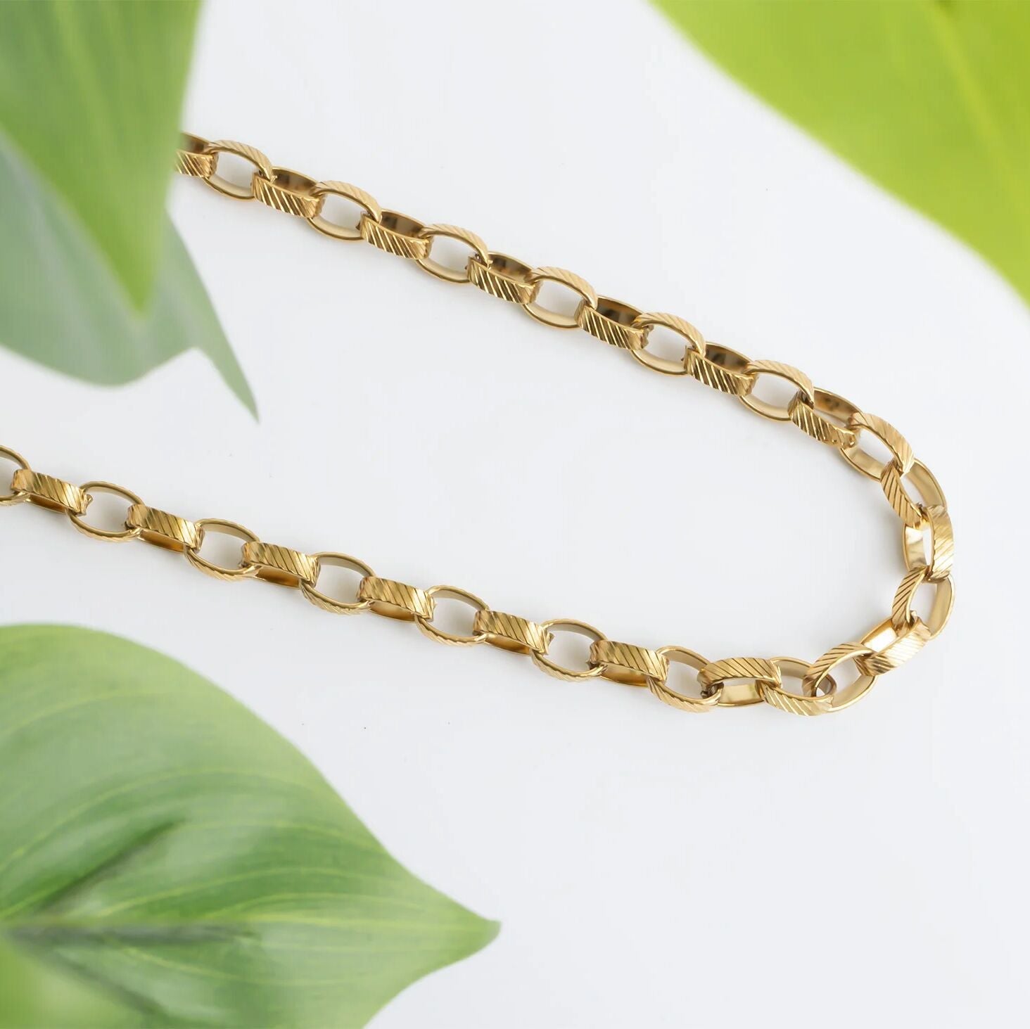 Gold chain necklace on a light background with green leaves