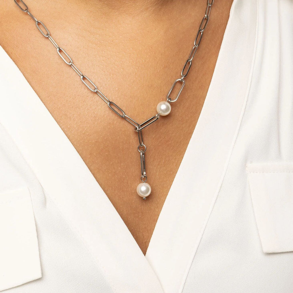 Silver y-shaped necklace with pearl pendants worn by a person in a white outfit