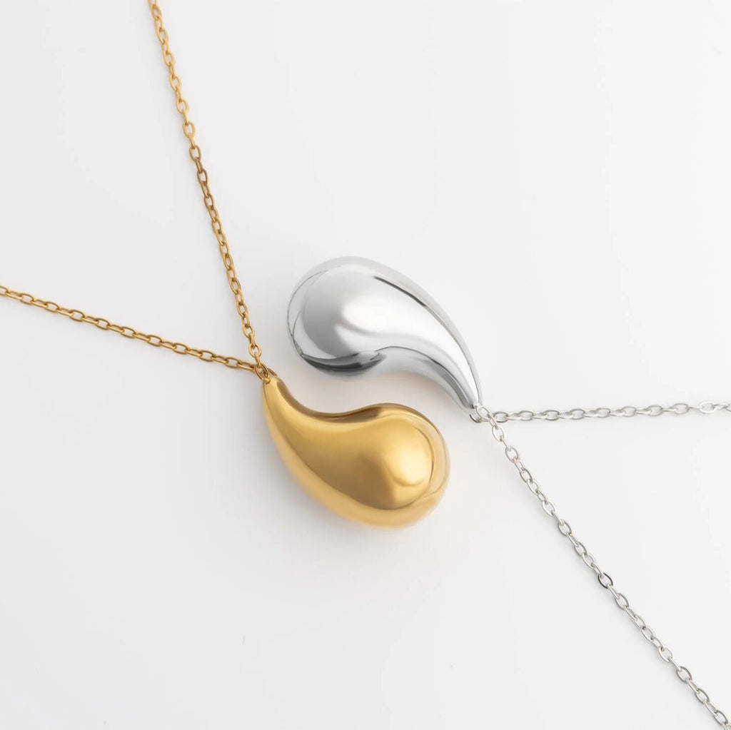 Two teardrop-shaped pendants on a gold and silver chain against a white background