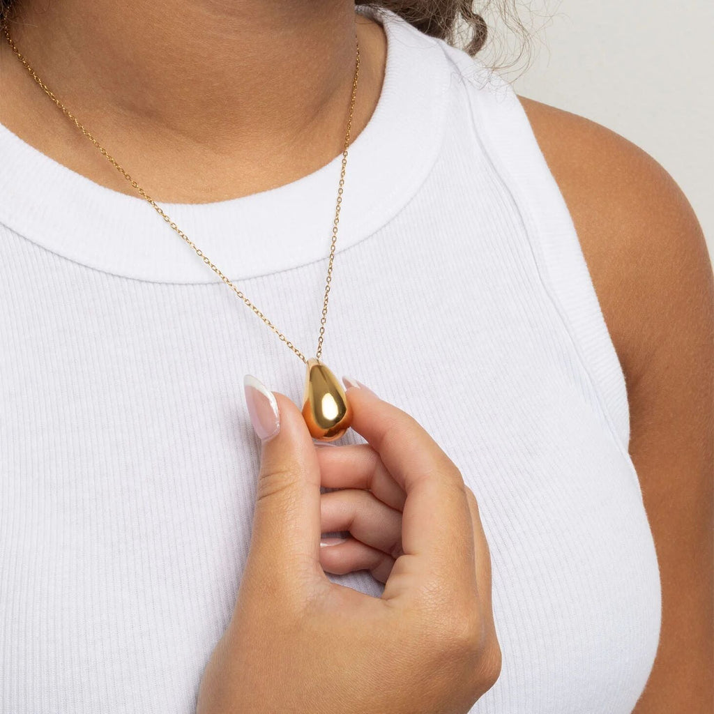 Person wearing a gold necklace with a pendant on a plain background