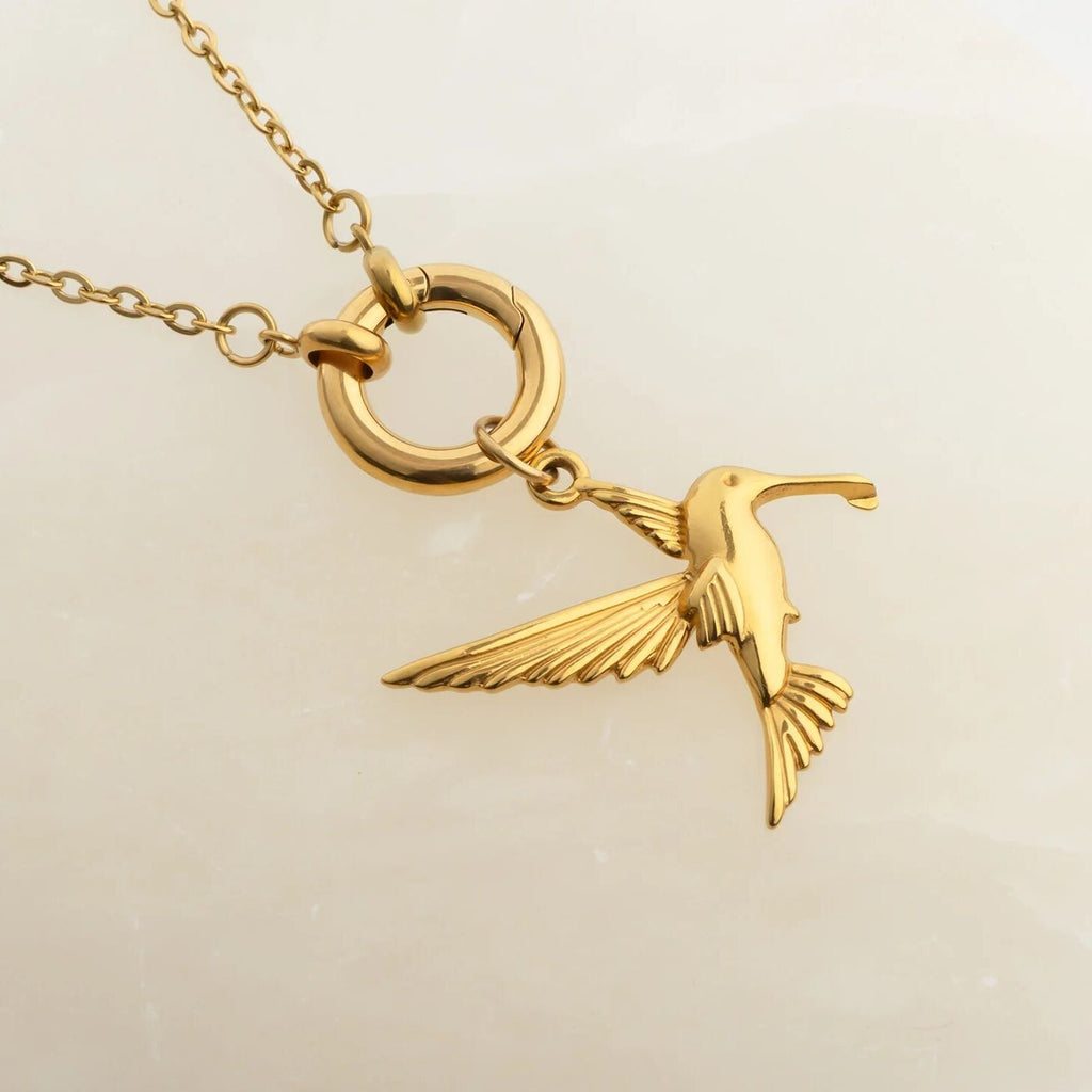 Gold bird pendant on a charm holder necklace against a beige background