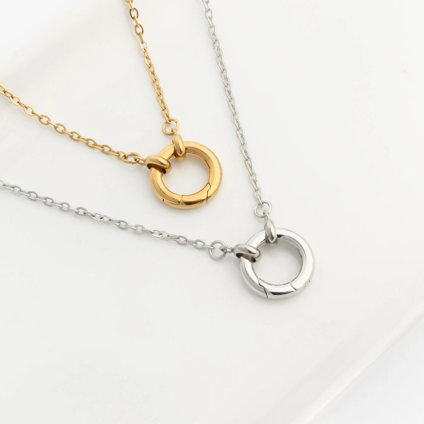 Two charm holder necklaces, one gold and one silver, on a light background.
