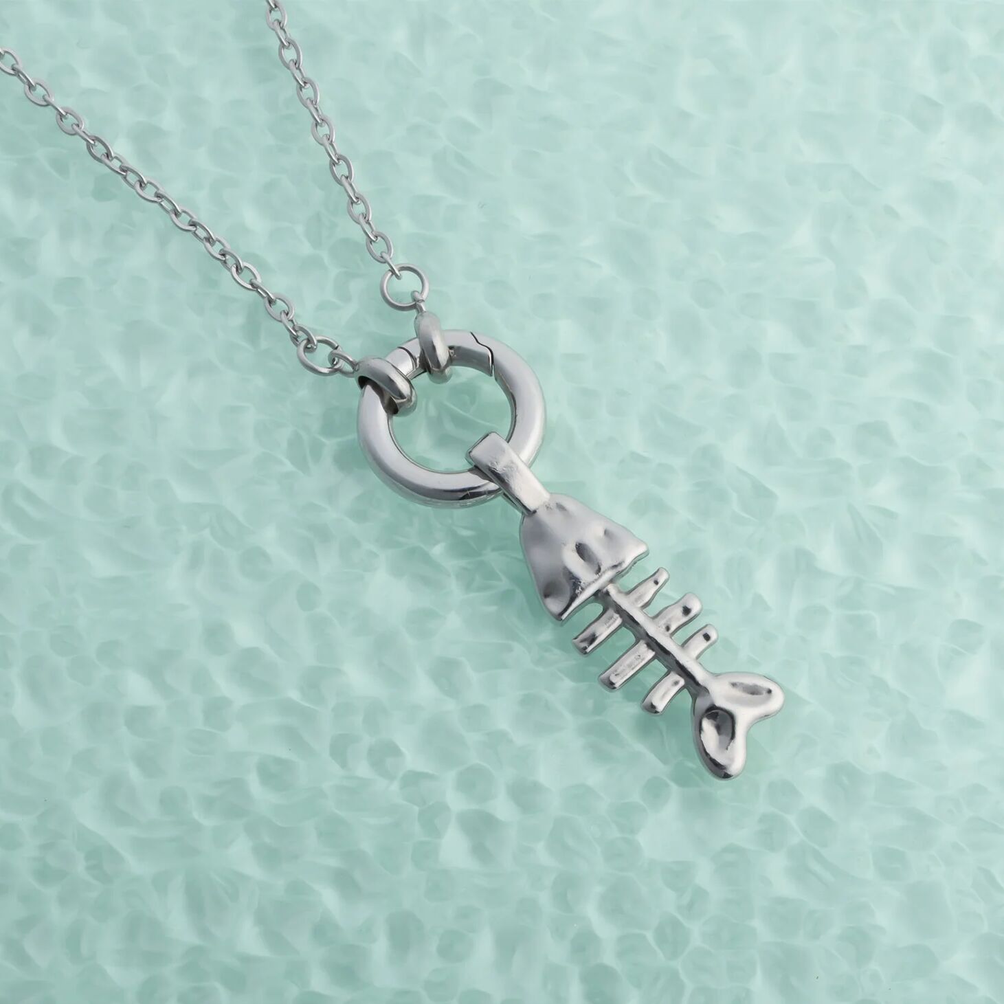 Silver charm holder necklace with a fish pendant on a light green textured background