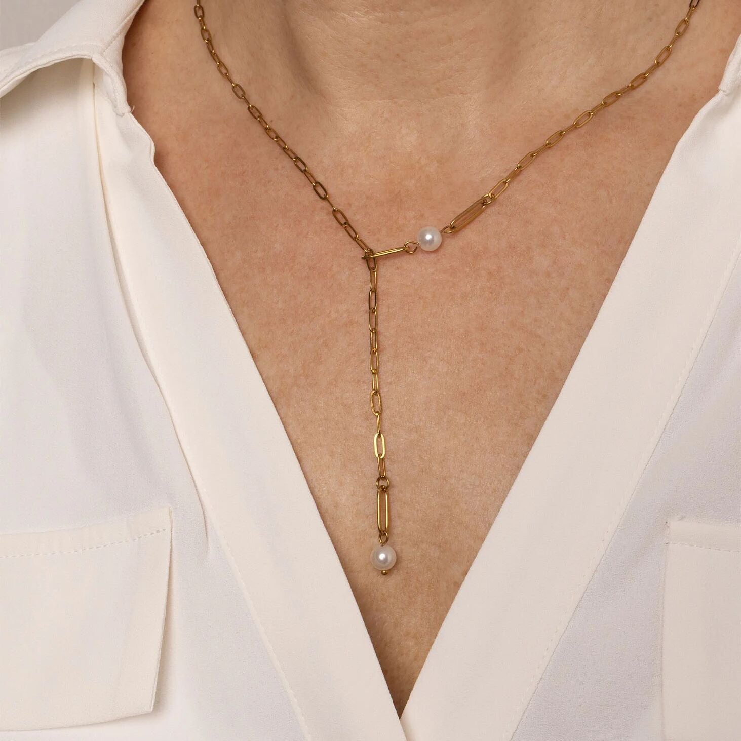 Gold y-shaped necklace with pearl drops worn by a person in a white blouse.
