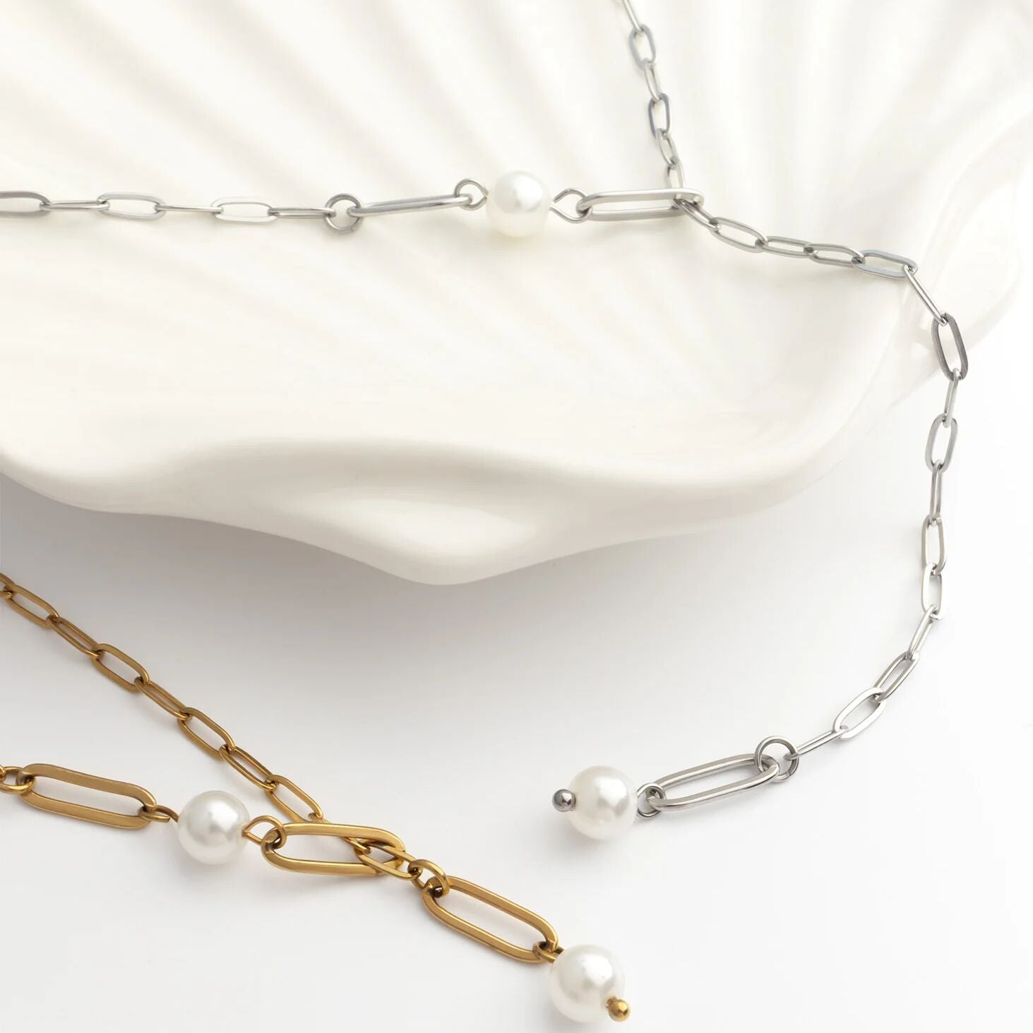 Two pearl necklaces, one gold and one silver, on a white background.