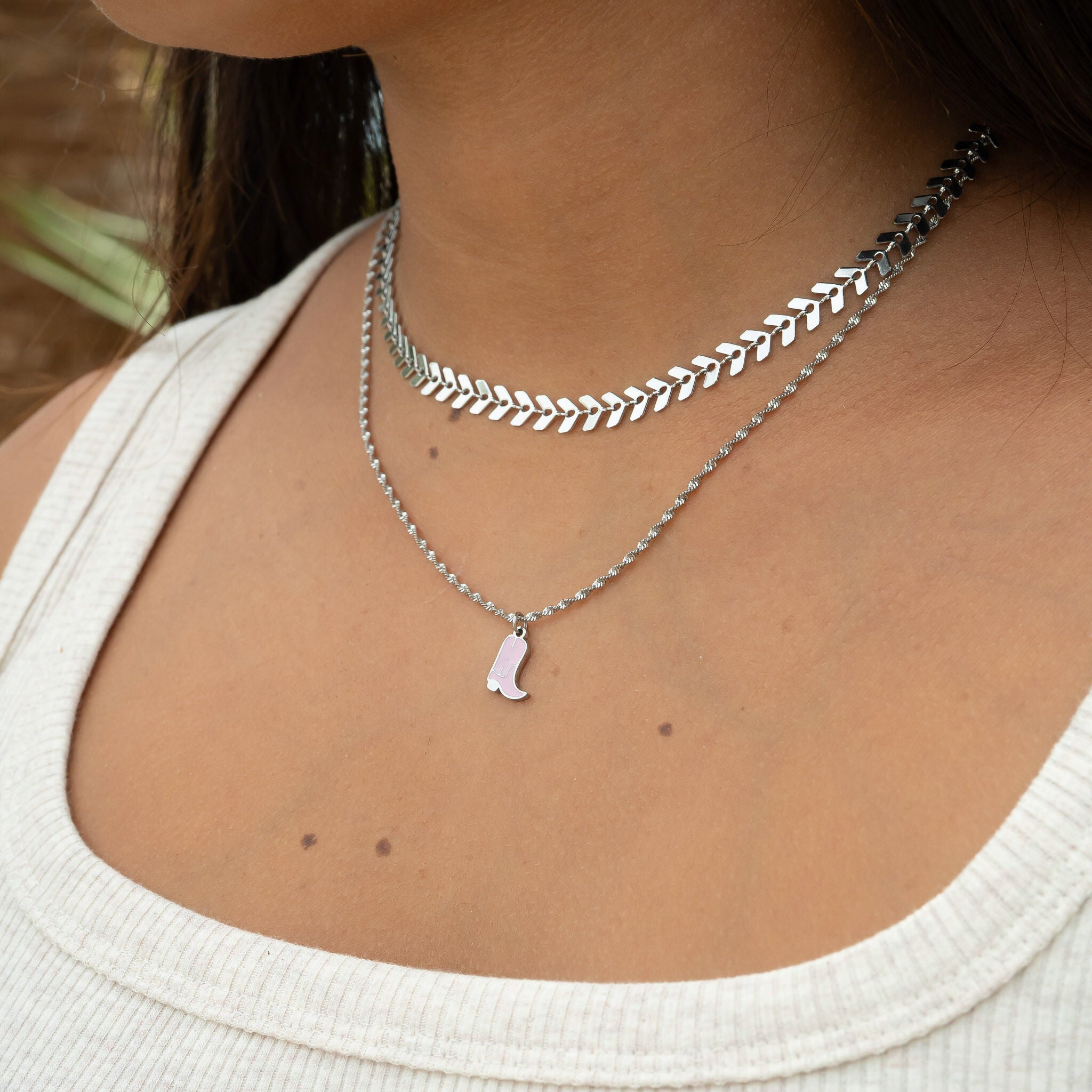 Close-up of a person wearing multiple silver necklaces with a white top.