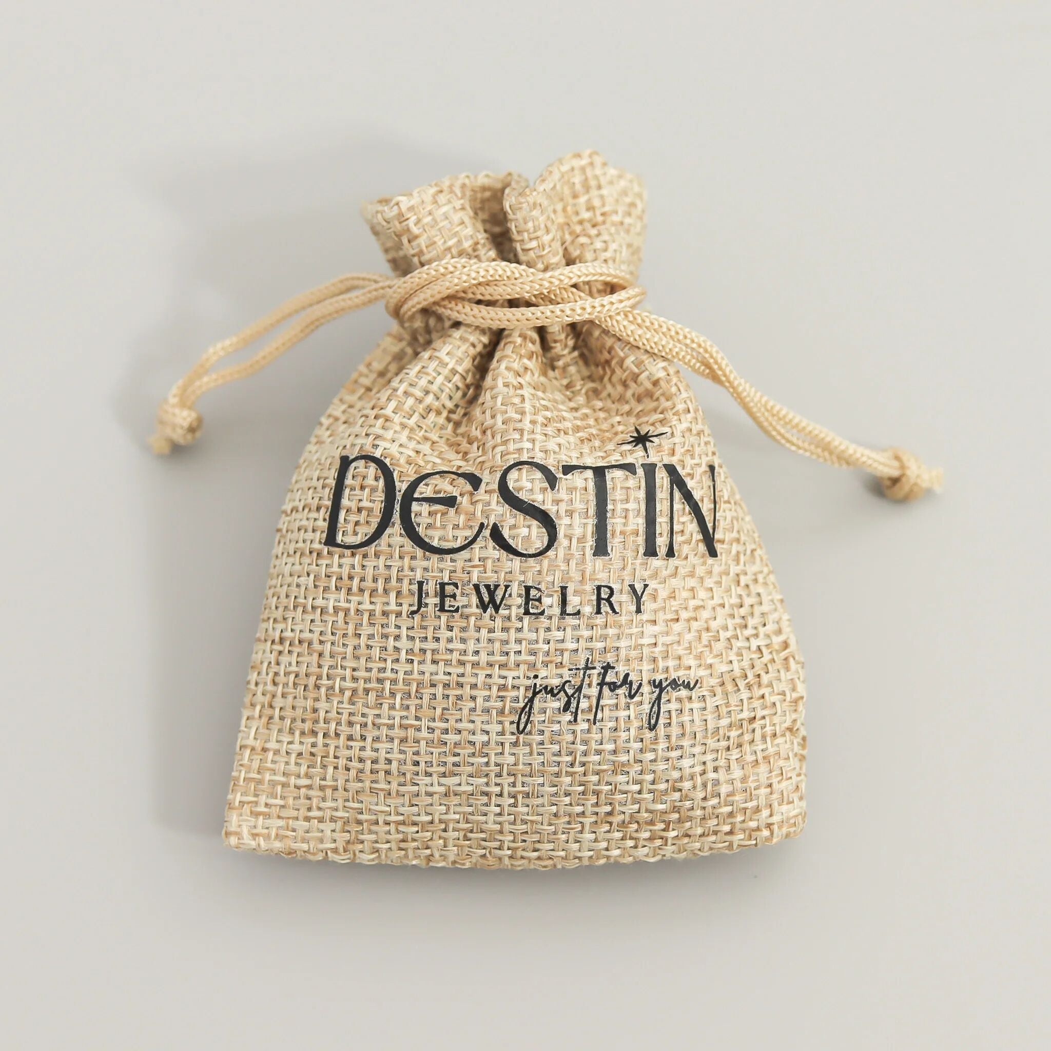 Jute drawstring bag with 'Destin Jewelry' branding on a gray background