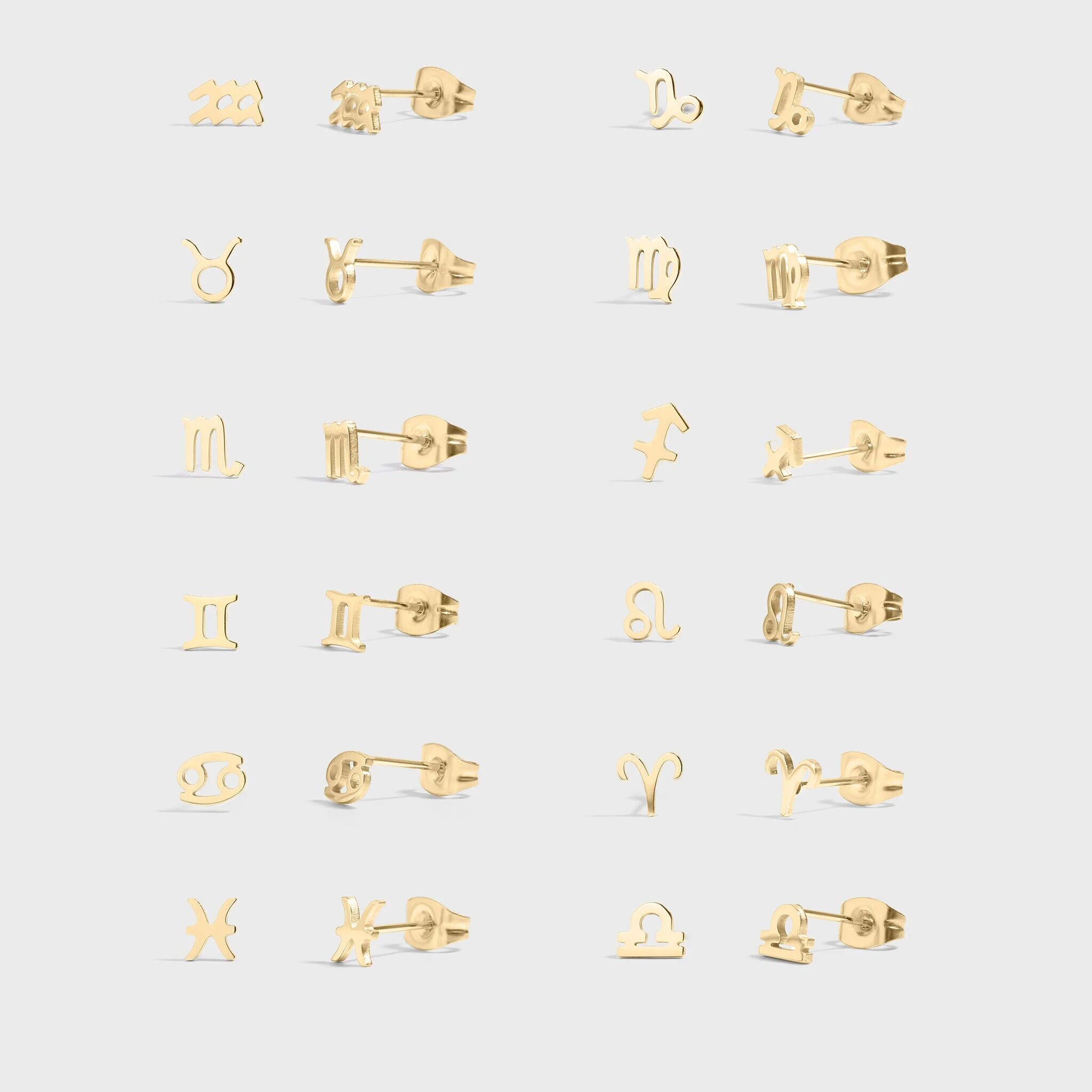 Set of gold earrings with zodiac symbols on a light gray background