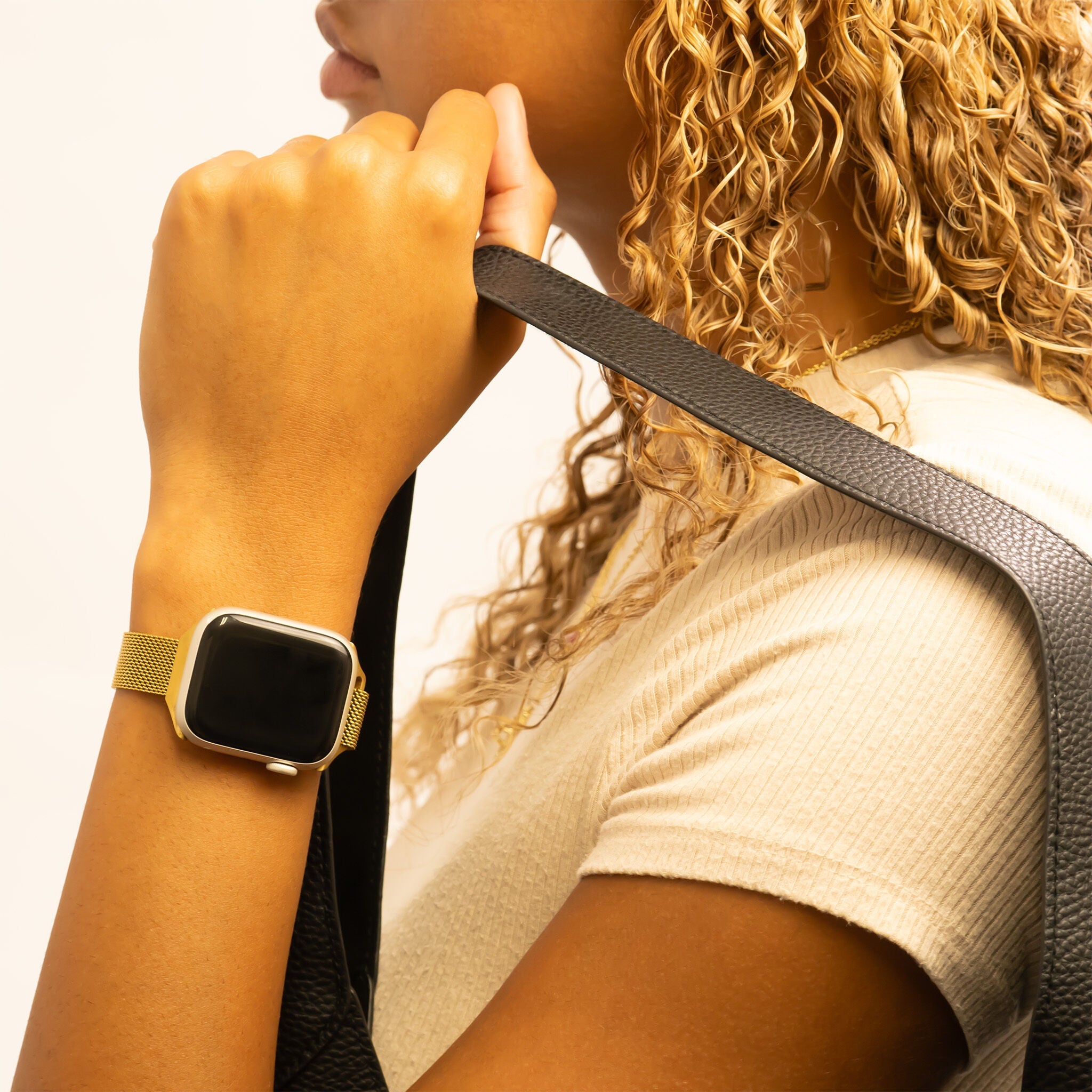 Person wearing a gold smartwatch and holding a black strap.