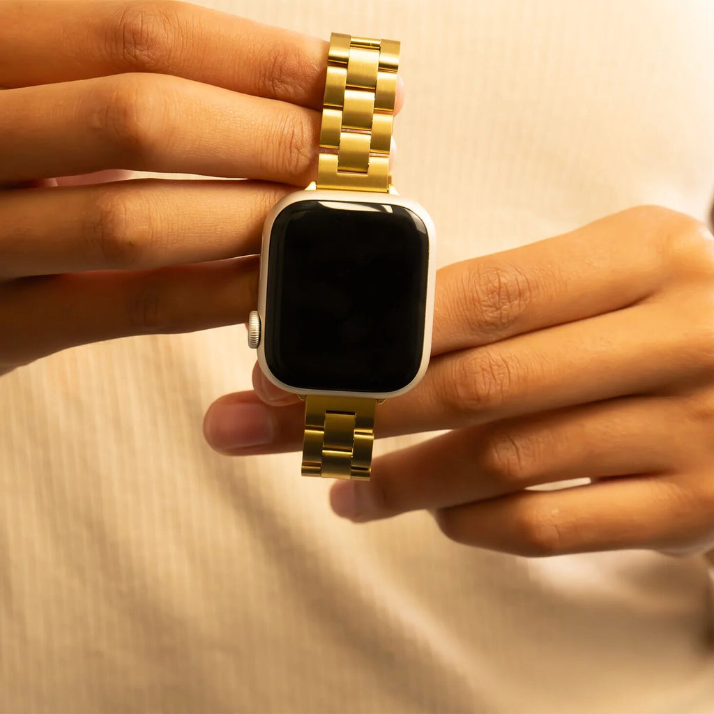 Smartwatch with a gold metal band held by a person's hand against a beige background