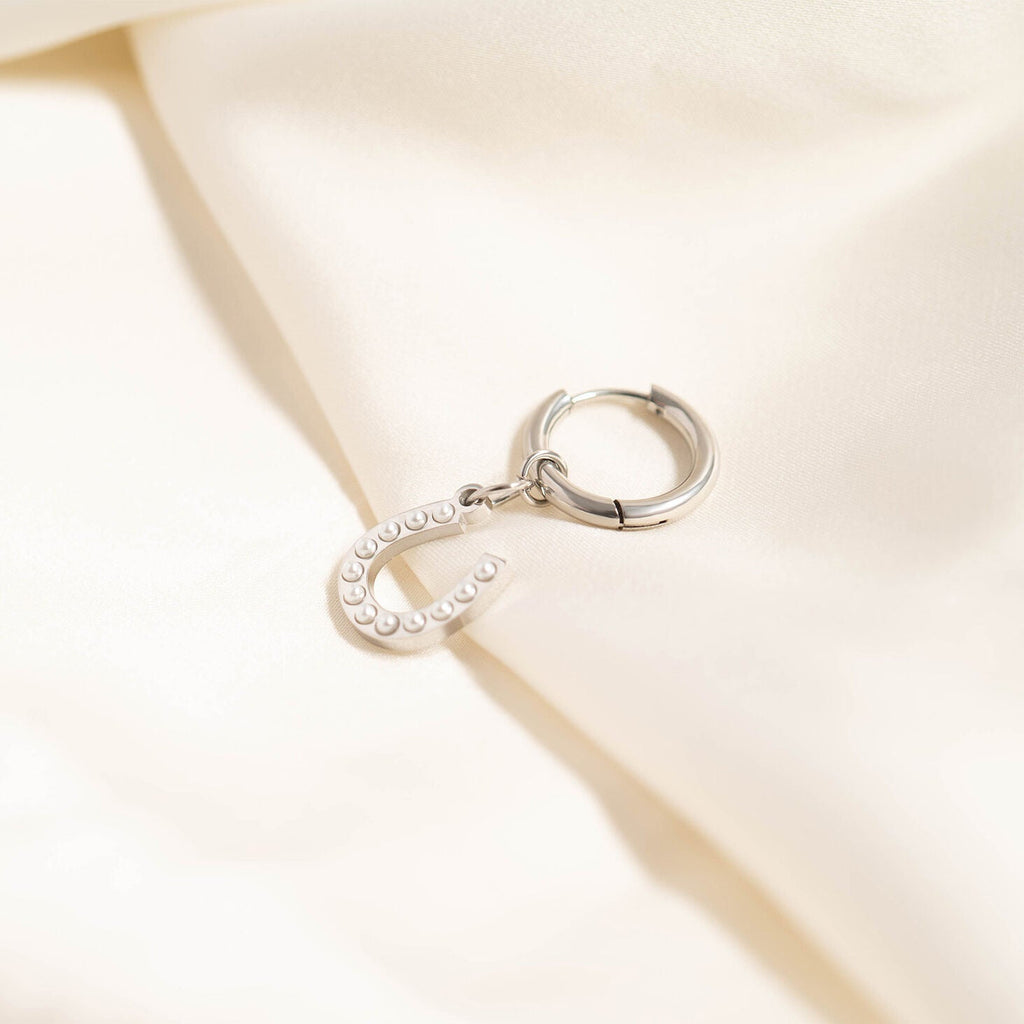 Silver hoop earring with a small round charm on a beige fabric background