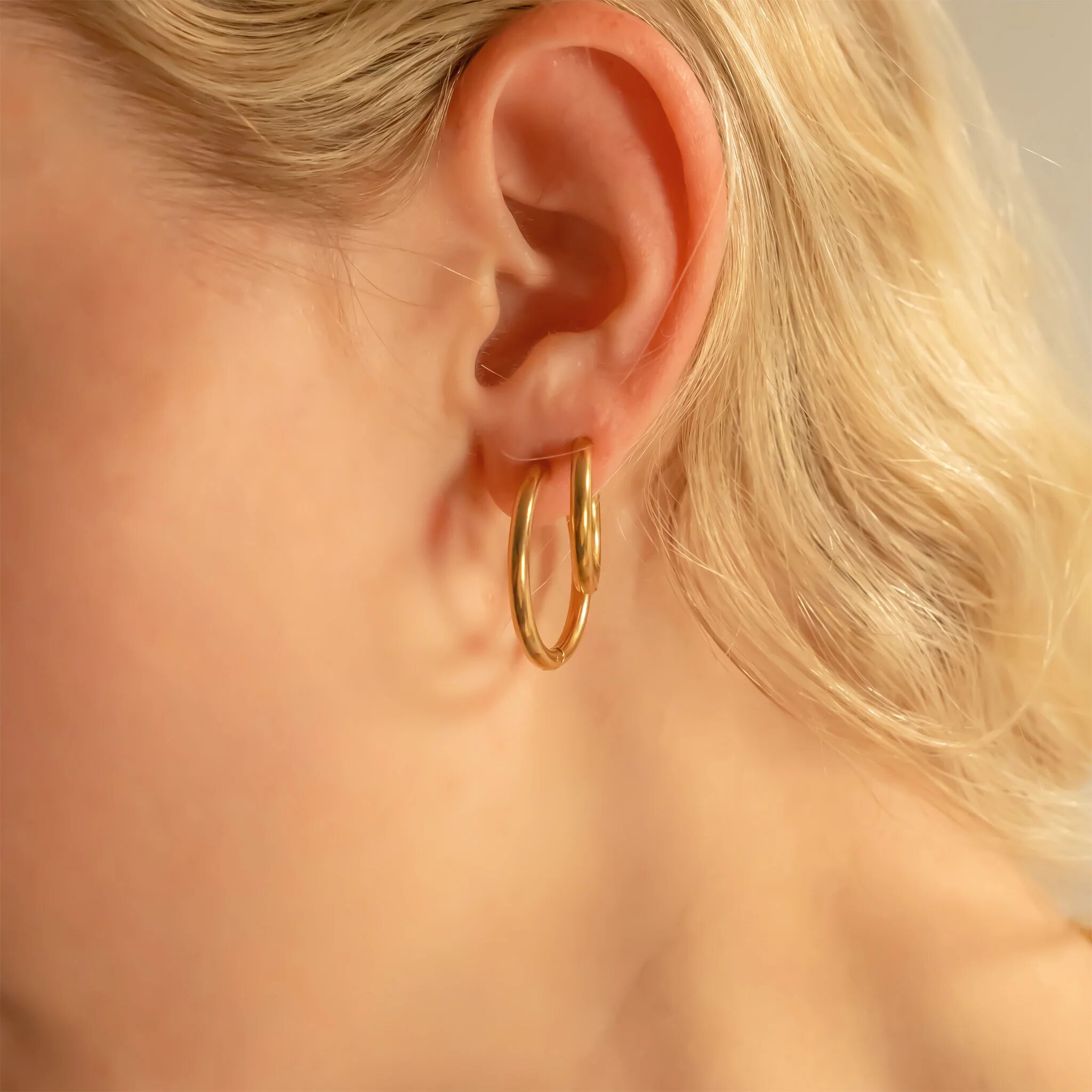 Close-up of an ear wearing a gold hoop earring with a blurred background