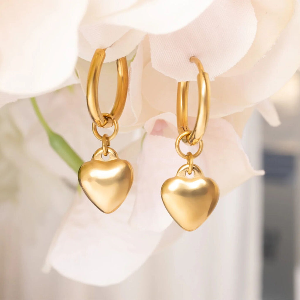 Gold heart-shaped earrings on a soft floral background