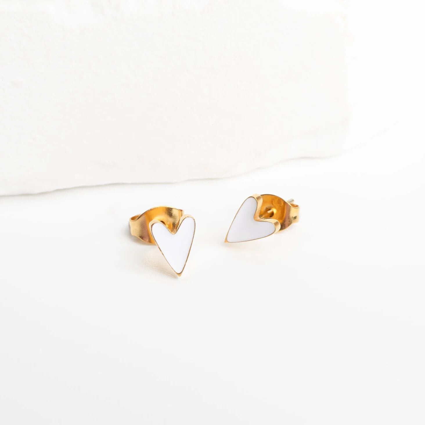 Heart-shaped gold and white earrings on a white background
