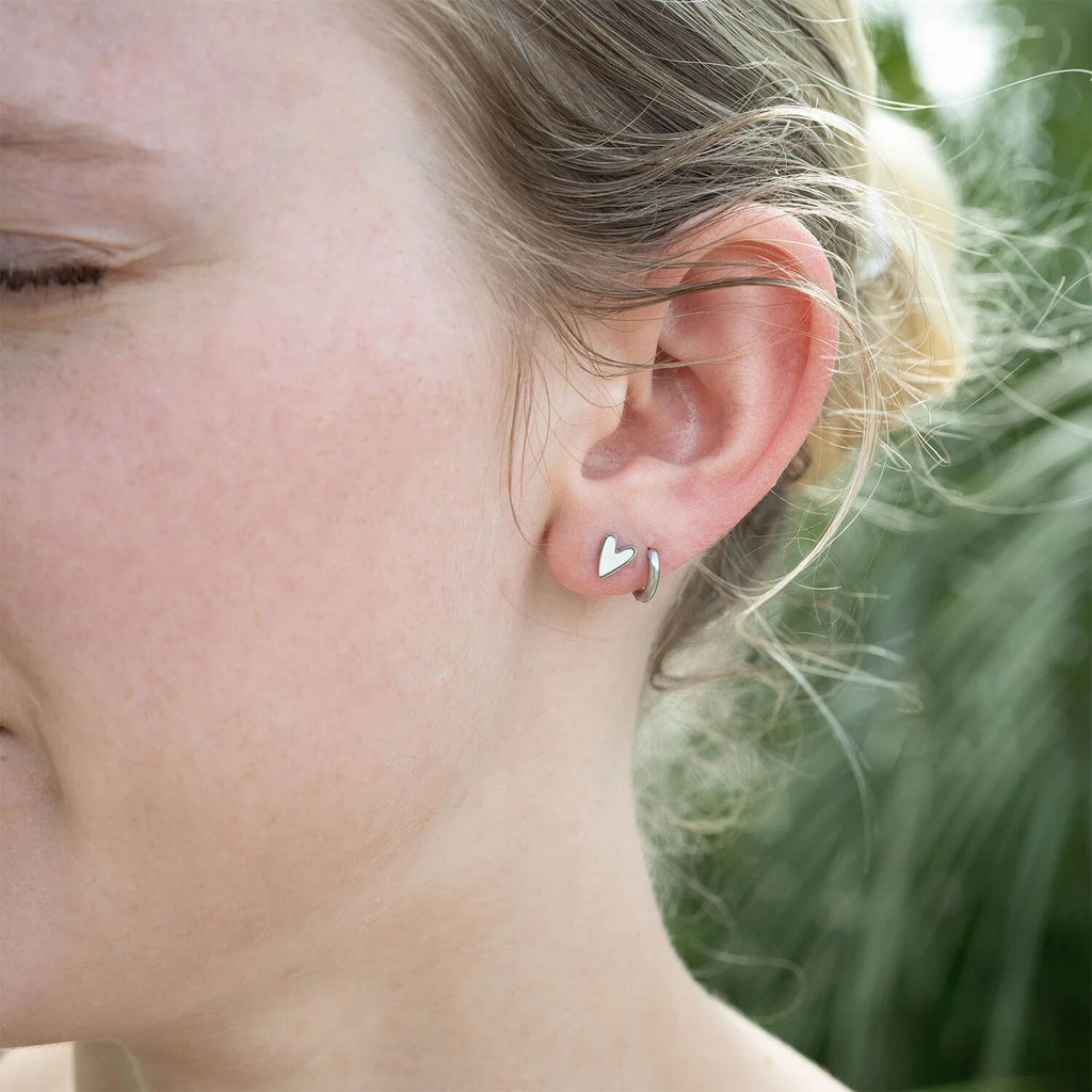 Close-up of a person wearing a heart-shaped earring with a blurred natural background