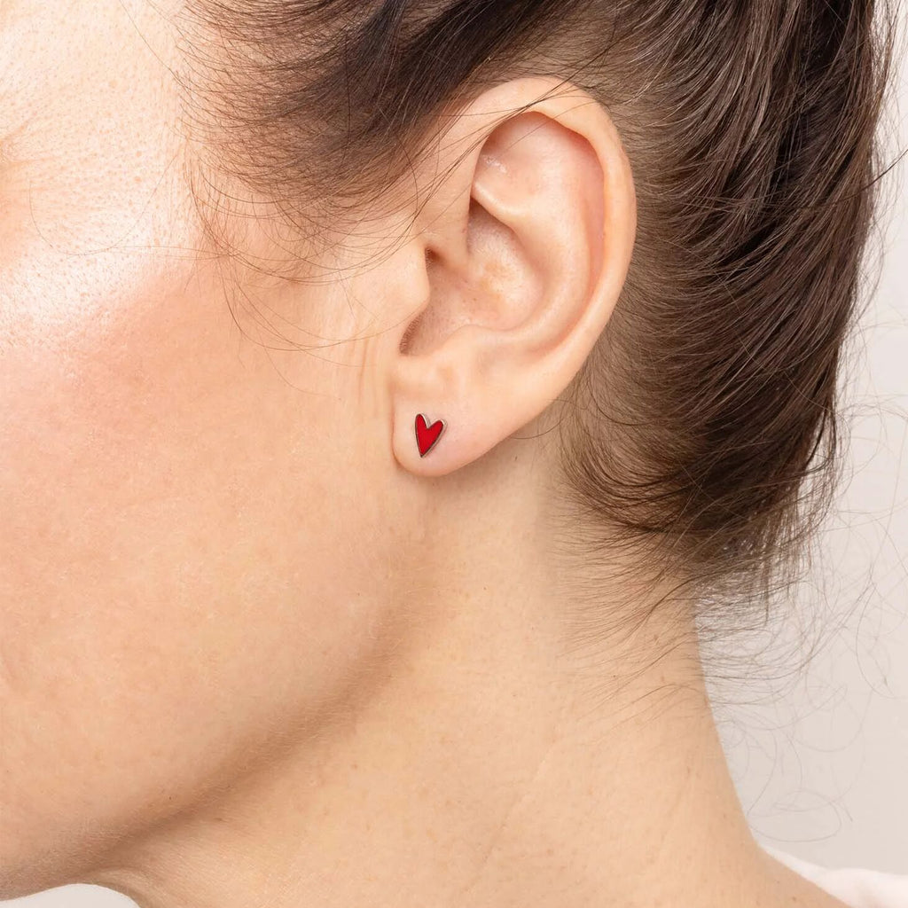 Close-up of an ear wearing a red heart-shaped earring with a neutral background