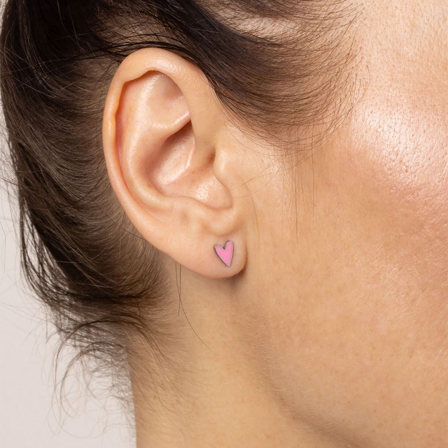 Close-up of an ear wearing a pink heart-shaped earring with blurred background