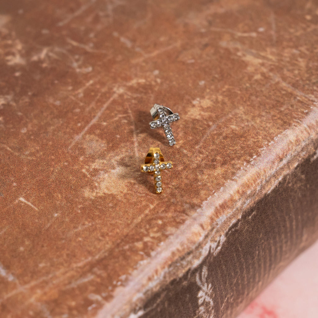 Two gold and silver small CZ stone stud earrings on a brown textured surface
