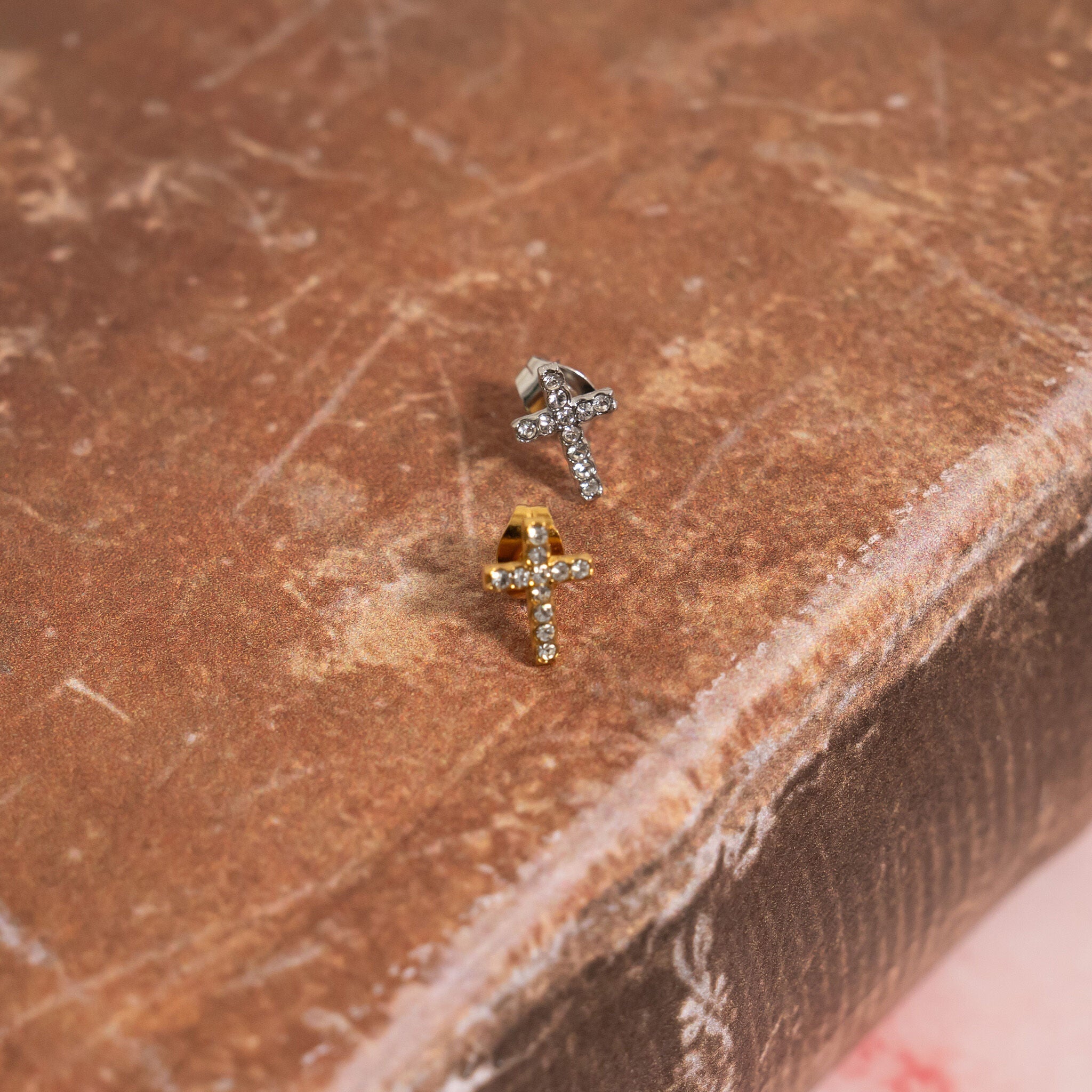 Two gold and silver small CZ stone stud earrings on a brown textured surface