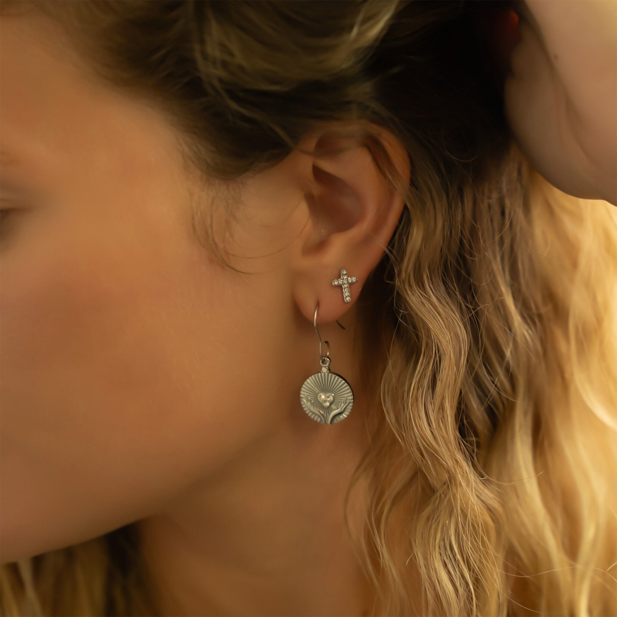 Close-up of a woman's ear wearing silver cross earrings with a blurred background