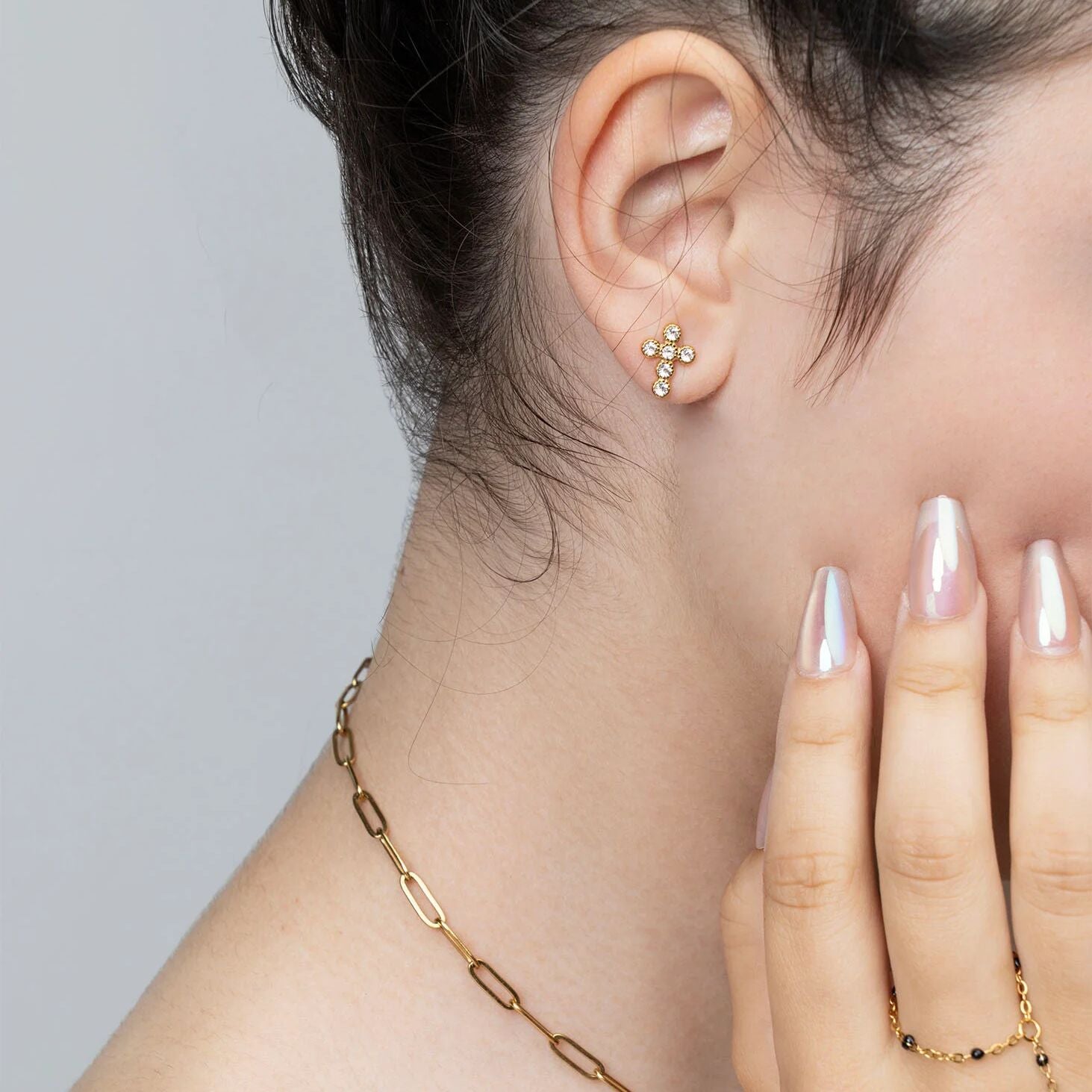 Close-up of a person wearing a gold earring and necklace with a neutral background
