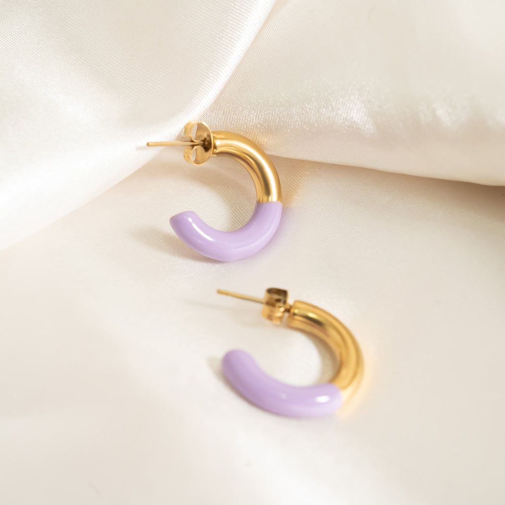 Gold and purple hoop earrings on a light beige surface